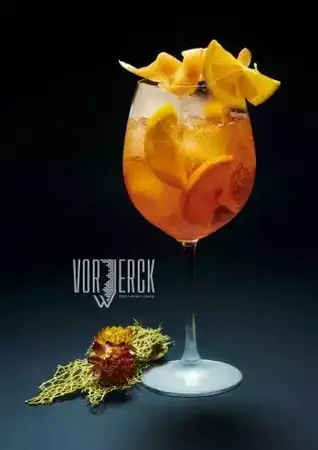 Aperol Spritz Cocktail mit Orangenscheiben und Eiswürfeln in Weinglas auf dunklem Hintergrund.