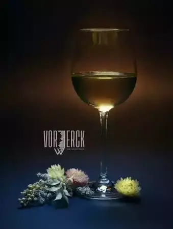 Ein Glas Weißwein steht auf einem Tisch, umgeben von dekorativen Trockenblumen.