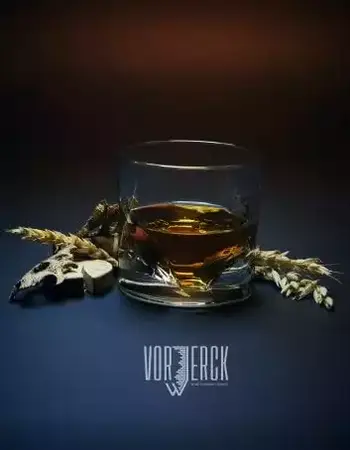 Ein Glas Whisky steht vor Ähren und Getreide auf dunklem Hintergrund, Logo „VORWERCK“.