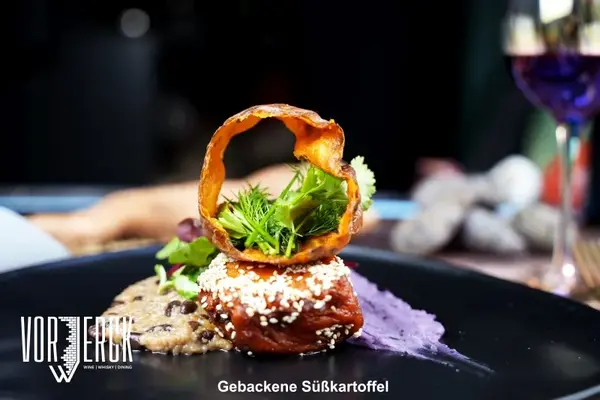 Kunstvoll angerichtete gebackene Süßkartoffel mit Sesam, Kräutern und violetter Creme.