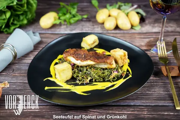 Seeteufelfilet auf Spinat und Grünkohl mit Kartoffeln und gelber Sauce auf schwarzem Teller.