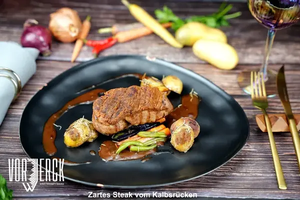 Zartes Kalbsrücken-Steak mit Kartoffeln, Gemüse und Bratensauce auf edlem Teller serviert.