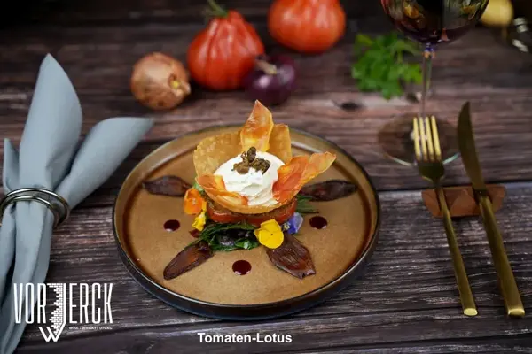 Kreativ angerichtetes Tomaten-Lotus-Gourmetgericht auf rustikalem Holztisch im Restaurant.