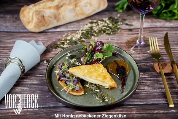 Mit Honig gebackener Ziegenkäse auf Salat, Brot, Kernen und Dip, serviert mit Wein.