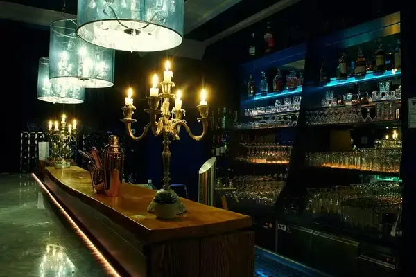 Stimmungsvolle Bar mit Kronleuchtern, beleuchtetem Tresen und gut gefülltem Spirituosenregal.