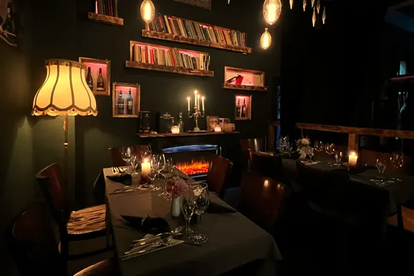 Gemütliches Restaurant mit Kerzenlicht, Kamin, Büchern und elegant gedeckten Tischen.