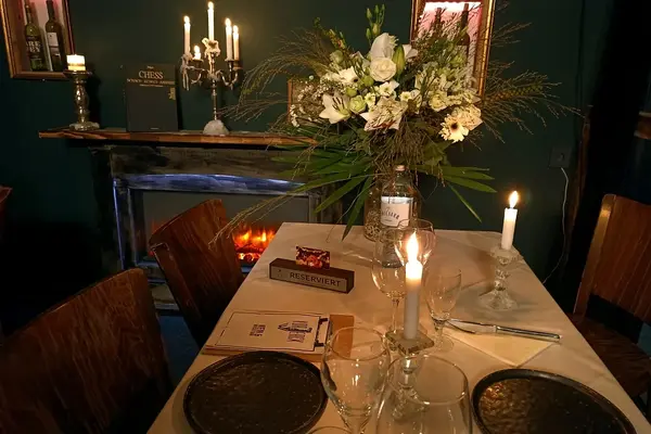 Stimmungsvoll gedeckter Tisch im Restaurant mit Kerzenlicht, Blumenstrauß und Kamin.