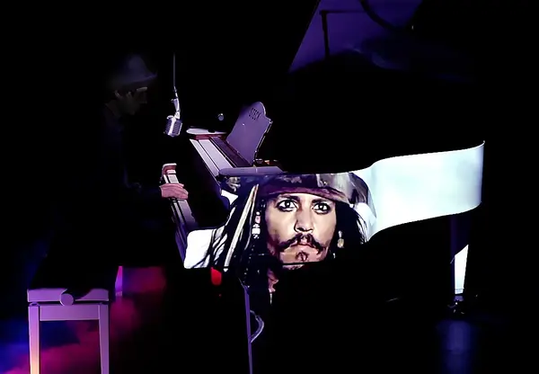 Ein Musiker spielt Klavier auf einer Bühne, das Piano zeigt ein Porträt von Jack Sparrow.