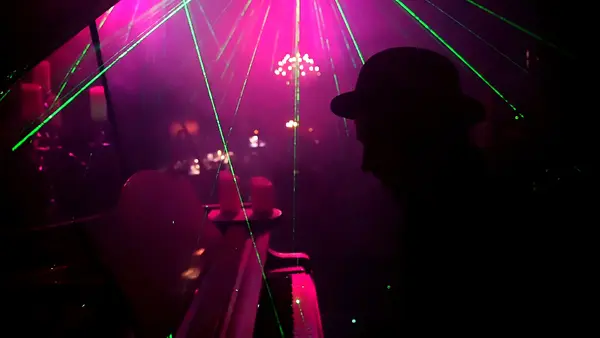 Silhouette eines Musikers am Klavier in einer Clubszene mit Laserlicht und lila Beleuchtung.