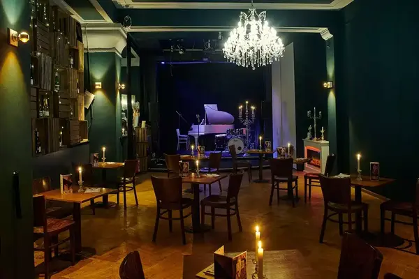 Gemütliches Café mit Kerzenlicht, Bühne, Flügel und stilvoller Einrichtung für Livemusik.