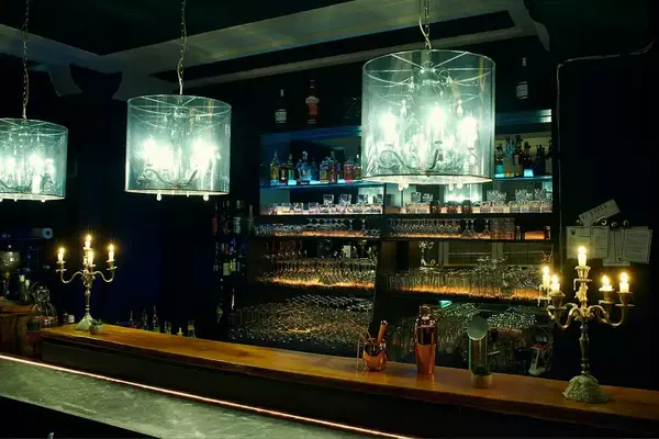 Stimmungsvolle Bar mit gläsernen Kronleuchtern, Kerzenlicht und gut bestücktem Regal.