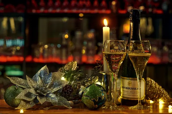 Festlich gedeckter Tisch mit Sektgläsern, Flasche Sekt, Kerze und Weihnachtsdekoration.